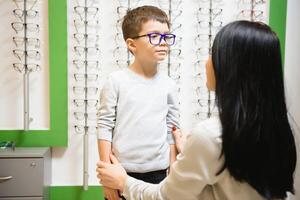 moeder met zoon kiezen bril in optiek op te slaan foto