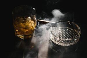 een glas van whisky of bourbon met ijs kubussen en een sigaar Aan een zwart leisteen met rook foto