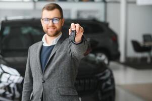 ja, dat is mijn nieuw auto. klant in auto dealerschap. jong Mens knielde naar beneden met sleutels in hand. foto