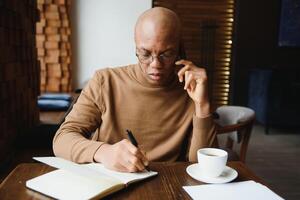 Afro-Amerikaans ondernemer vervelend overhemd met gerold omhoog mouwen op zoek door venster met attent en echt gezicht uitdrukking, gevoel nerveus voordat vergadering met bedrijf partners Bij cafe. foto