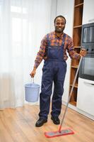 professioneel schoonmaakster in blauw uniform het wassen verdieping en afvegen stof van de meubilair in de leven kamer van de appartement. schoonmaak onderhoud concept foto