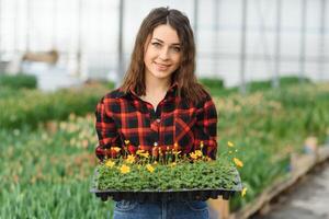 mooi jong glimlachen meisje, arbeider met bloemen in serre. concept werk in de serre, bloemen, tulpen, doos met bloemen. kopiëren ruimte. foto