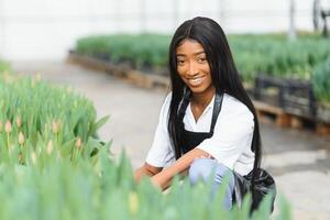 mooi jong glimlachen Afrikaanse Amerikaans meisje, arbeider met bloemen in serre. concept werk in de serre, bloemen. foto