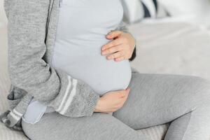 mooi zwanger vrouw houdt handen Aan buik in slaapkamer Bij huis. jong moeder aan het wachten van een baby. concept van zwangerschap, moederschap, Gezondheid zorg, gynaecologie, geneesmiddel. detailopname, binnenshuis. foto