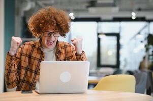 portret van Kaukasisch mannetje freelancer in modieus kleding zittend Bij cafetaria tafel en aan het doen afgelegen werk voor programmering ontwerp van openbaar website, geschoold software ontwikkelaar poseren in coworking ruimte. foto