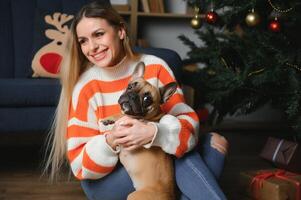 mooi vrouw zit Aan een wijnoogst bankstel met hond. Aan een achtergrond van een Kerstmis boom in een versierd kamer. gelukkig nieuw jaar foto