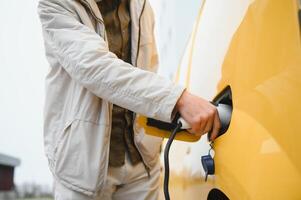 Mens Holding macht opladen kabel voor elektrisch auto in buitenshuis auto park. en hij s gaan naar aansluiten de auto naar de opladen station in de parkeren veel in de buurt de boodschappen doen centrum foto