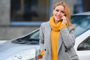 vrouw met een mobiel telefoon in de buurt opladen elektrisch auto. voertuig opladen Bij openbaar opladen station buitenshuis. auto sharing concept foto