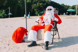 de kerstman claus in zonnebril drankjes een cocktail terwijl aan het liegen Aan een zon ligstoel Aan de meer strand. de kerstman in de tropen foto