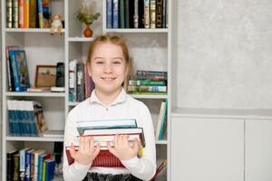 blij meisje met een stack van boeken in haar handen tegen de achtergrond van een boekenplank foto