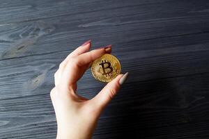 bitcoin goud munt in vrouw hand- Aan de donker blauw houten achtergrond. foto