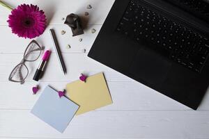laptop, kleurrijk memo lakens, bril, stylus, roze gerbera en elementen van decoratie Aan een wit houten werk bureau. mooi vrouw werkplaats top visie. foto