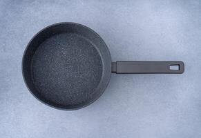 nieuw graniet frituren pan Aan een grijs achtergrond, top visie. leeg bakken pan met handvat. foto