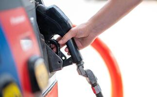 vrouw arbeider hand- Holding mondstuk brandstof vullen olie in auto tank Bij pomp gas- station foto