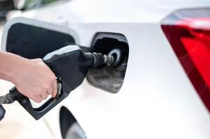 vrouw arbeider hand- Holding mondstuk brandstof vullen olie in auto tank Bij pomp gas- station foto