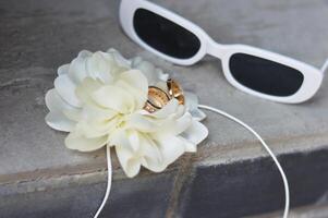 zonnebril, wit boutanier bloem en pasgetrouwden ringen Aan een grijs beton oppervlak. bruiloft accessoires. foto