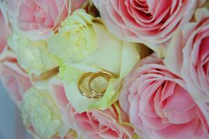 bruiloft boeket van roze en wit rozen en bruiloft ringen aan het liegen Aan bloem bloemblaadjes. foto