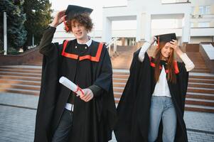 gelukkig vrienden Aan diploma uitreiking dag. portret van twee vrolijk blij studenten staand in de buurt Universiteit gebouw. foto