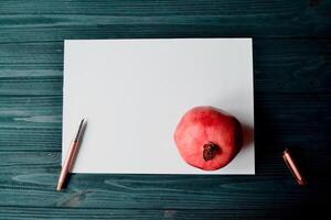 de vel van wit papier met pen en granaat Aan de donker blauw houten bureau. wijnoogst achtergrond met plaats voor tekst. foto