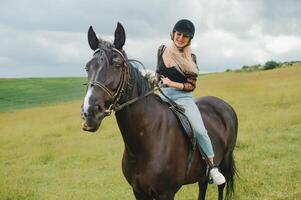 jong vrouw rijden een paard Aan de groen veld- foto