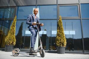 knap Afrikaanse Jaren 30 Mens vervelend jas glimlachen terwijl rijden elektrisch scooter buitenshuis foto