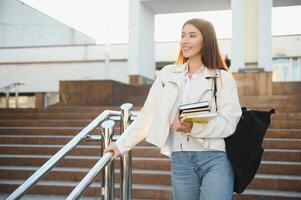 jong meisje leerling glimlachen tegen Universiteit. schattig meisje leerling houdt mappen en notebooks in handen. aan het leren, onderwijs concept foto