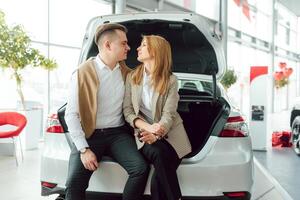 gelukkig jong paar kiest en buying een nieuw auto voor de familie in de handel foto