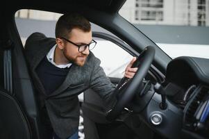 bezoekende auto dealerschap. knap gebaard Mens is strelen zijn nieuw auto en glimlachen foto