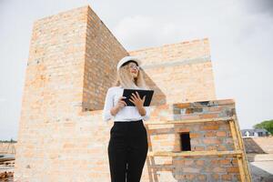 geabsorbeerd in de werk van een vrouw ingenieur werken met een tablet Aan de achtergrond van de bouw plaats. portret van een jong architect, beschermend apparatuur. selectief focus foto