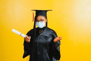 portret van een jong Afrikaanse leerling in een afstuderen pet beschermend masker, Aan een geel achtergrond, diploma uitreiking 2021 foto