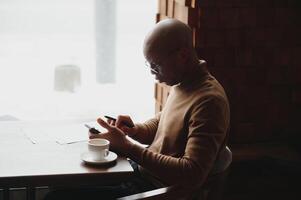 kennis, aan het leren, onderwijs en technologie. terloops gekleed hard werken een student met afro kapsel oplossen wiskundig problemen, zittend Bij cafe tafel met leerboeken en elektronisch apparaat. foto