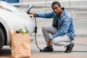 Afrikaanse Amerikaans Mens opladen zijn elektrisch auto. foto