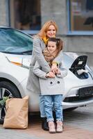 elegant moeder en dochter in rekening brengen een elektrisch auto, en besteden tijd samen foto