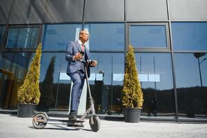 zakenman met elektrisch scooter staand in voorkant van modern bedrijf gebouw pratend Aan telefoon. foto