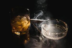 een glas van whisky of bourbon met ijs kubussen en een sigaar Aan een zwart leisteen met rook foto