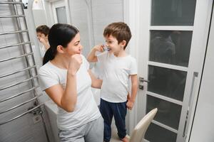 mooi moeder en gelukkig zoon poetsen tanden in de buurt spiegel in badkamer foto