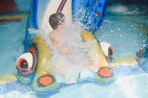 de jongen is rollend met een water glijbaan Bij een water park in weinig rots foto