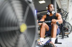 gemotiveerd jong zwart sportman hebben training Aan roeien machine foto