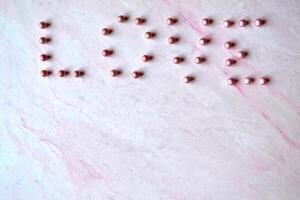 de woord liefde gelegd uit met kralen Aan de roze getextureerde achtergrond. foto