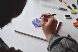 vrouw verven in een schetsboek. gereedschap voor schilderij Aan de wit houten bureau. schilder werk. foto