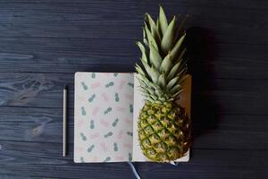 ananas en notitieboekje Aan de donker blauw houten tafel. abstract elegant achtergrond. foto