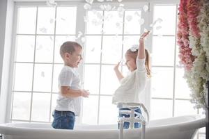 kind spelen met rozenblaadjes in huis badkamer. klein meisje en jongen samen plezier en vreugde. het concept van de kindertijd en de realisatie van dromen, fantasie, verbeelding foto