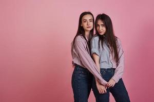 jonge vrouwen die plezier hebben in de studio met roze achtergrond. schattige tweeling