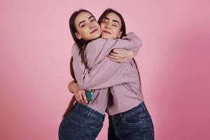 familie knuffels tussen twee zussen in identieke kleding in de studio met roze achtergrond
