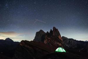 vallende sterren aan de blauwe hemel. nacht foto van seceda dolomieten bergen. toeristen rusten in de groene tent