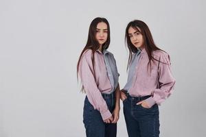 twee zussen tweeling staan en poseren in de studio met witte achtergrond foto