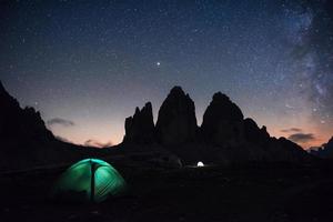 beetje mist over de rotsen. twee verlichtingstenten met toeristen binnen in de buurt van de tre cime drie pieken bergen 's nachts foto