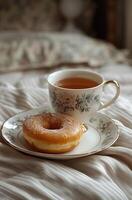 ai gegenereerd een kop van thee en een donut is getoond Aan een bed naar tonen de ontbijt visie foto