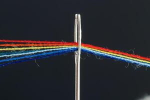 veelkleurig draden voor naaien in de het formulier van een regenboog voorbij gaan aan door een antiek naald- Aan een zwart achtergrond foto