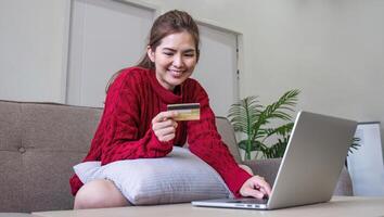 online winkelen. vrouw buying laptop gebruik makend van credit kaart zittend Aan sofa Bij huis foto